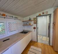 A kitchen in a cottage with a wooden ceiling, white walls, and decorated shelves.
