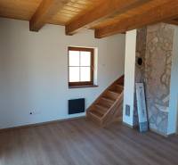 Interior of a cabin with a wooden ceiling, stairs, and a stone wall.