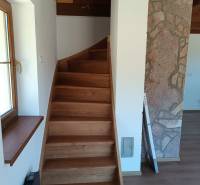 Wooden stairs in a cabin with a stone wall and a window.