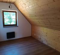 Attic room with wooden paneling, a window, and simple lighting in a cabin.