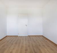 An empty room with wooden flooring and white walls in a 3-room apartment.