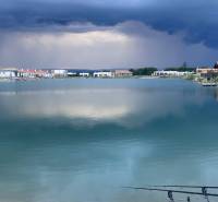 A lake surrounded by houses in Boldog, residential plots, dramatic sky before a storm.