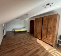 Attic room in a family house with a bed, wardrobes, and wooden floor.