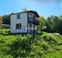 A cottage in Počúvadlo surrounded by greenery, with a balcony and a garden on a slope.