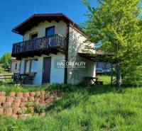 A cottage in Počúvadlo with a wooden balcony and greenery on the slope.