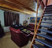 The interior of a cabin with a wooden ceiling, sofas, and a staircase leading to the upper floor.