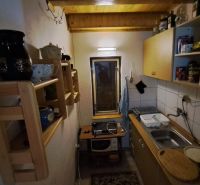 A narrow kitchen in a cabin with a wooden ceiling, shelves, and basic equipment.