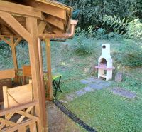 A wooden gazebo with a grill at the cottage in Dobrá, Kvakovce, surrounded by greenery and trees.