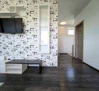 Interior of a 2-room apartment with a television on a patterned wall and dark flooring.