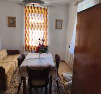 Dining room in a family house with a table, chairs, flowers, carpet, and curtain.