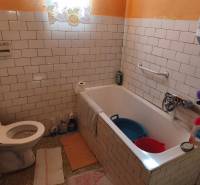 Bathroom in a family house with white tiles, a bathtub, and a toilet.