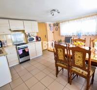 A kitchen in a family house with a large table, wooden chairs, and appliances.