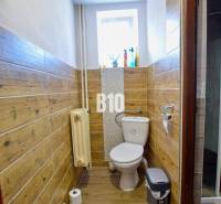 A bathroom with wooden paneling in a family house, window, radiator, and basic equipment.