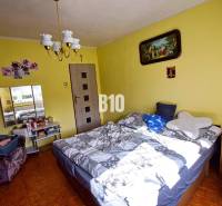 A bedroom in a family house with yellow walls, a bed, and wall decorations.