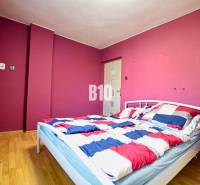 A bedroom with a light-colored bed, colorful walls, and parquet flooring in a family house.
