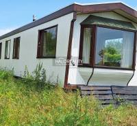 Boleráz: A cabin surrounded by nature with a glass veranda, grassy surroundings, and pallet stairs.
