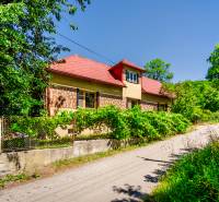 A family house on a quiet street in Púchov with lush greenery and a fence.