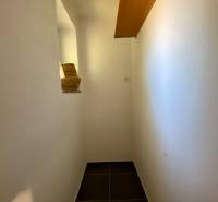 A narrow hallway with a bright sign in a 2-room apartment, a basket, and shelves on the wall.