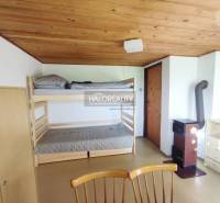 An interior with a bunk bed, wooden ceiling, wardrobe, and stove in Záhrady.