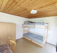 A simple room with a wooden panel ceiling, a bunk bed, and a wardrobe in the garden.