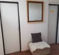Interior of a building with a hallway, mirror, doors, and a seat with a cushion.