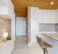 Brick wall in the kitchen of a two-room apartment with white furniture and marble floor.