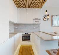 A kitchen in a 2-room apartment with white cabinets, brick detail, and natural stone.