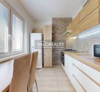A kitchen in a 3-room apartment with built-in appliances, wooden cabinets, and a dining table.