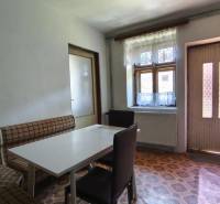 Interior of a family house with a table, chairs, and a seating bench, simple kitchen.