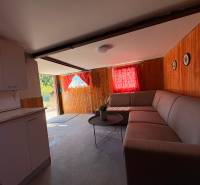 An interior with a corner sofa and a kitchen unit, wooden paneled walls, red curtains.