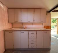 Simple kitchen unit in the interior, with cabinets and a sink, doors lead to the garden.