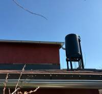 A roof with a water tank and details of gutters in the garden under the blue sky.