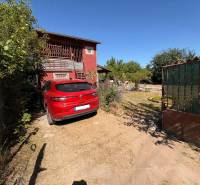 Gardens in Komárno with a red car, a house, and greenery behind the gate.