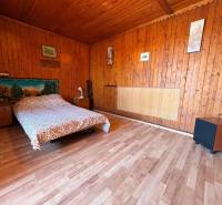 Wooden interior with a bed, decorative fabric on the wall, paintings, and simple furniture.