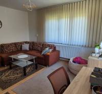 Living room with a brown sofa, glass table, and vertical blinds in a family house.
