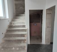 A staircase and an unfinished bathroom in a family house with gray tiles and white walls.