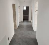 A hallway in a family house with white walls and gray tiles, without doors.
