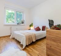 A bedroom in a 3-room apartment with wooden flooring and a view of greenery.