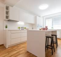 A kitchen in a 3-room apartment with wooden flooring, white cabinets, and a central island.