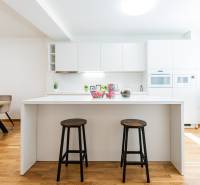 A kitchen in a 3-room apartment with a white kitchen unit, bar stools, and a wooden floor.