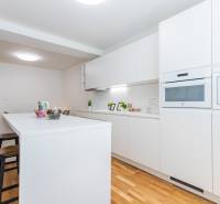 A kitchen in a 3-room apartment with white furniture and bar stools on a wooden floor.