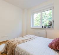 Bright bedroom in a 3-room apartment with a bed, blanket, and a window overlooking greenery.