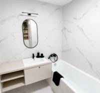 Bathroom in a 2-room apartment with a mirror and a bathtub, white marble tiles.