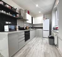 A kitchen in a 2-room apartment with white furniture, appliances, and black tiles.