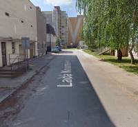 L. Novomeský Street in Pezinok with garages, residential buildings, and greenery.