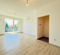 A bright living room with wooden flooring and balcony doors in a two-room apartment.