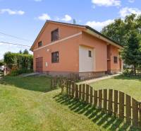 An orange cottage in the village of Kuchyňa with a wooden fence surrounded by greenery.