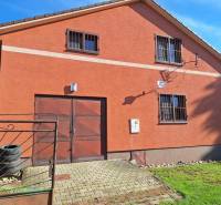 A cottage in Kuchyňa with an orange facade, a garage, and a garden on a sunny plot.