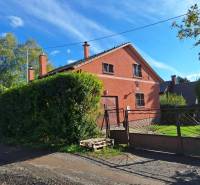 A cottage in the kitchen with a red facade behind a hedge and a metal gate.