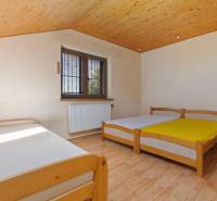 A room in a cottage with a wooden ceiling, three beds, and a window.